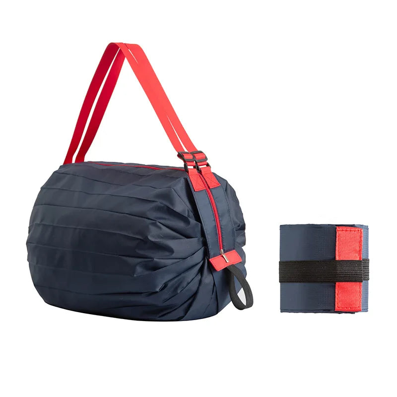 Navy blue Oxford shopping bag with bold red straps, displayed alongside its compact folded form secured by a black elastic band